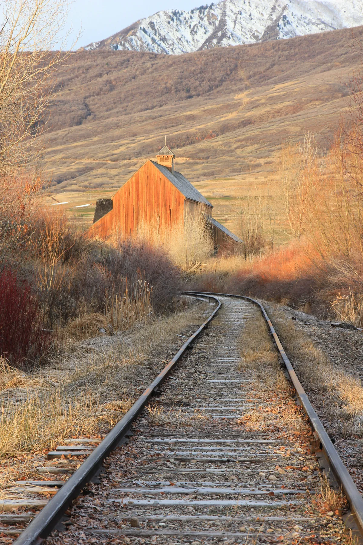 Railroad tracks curving toward a red barn beneath the Wasatch Mountains