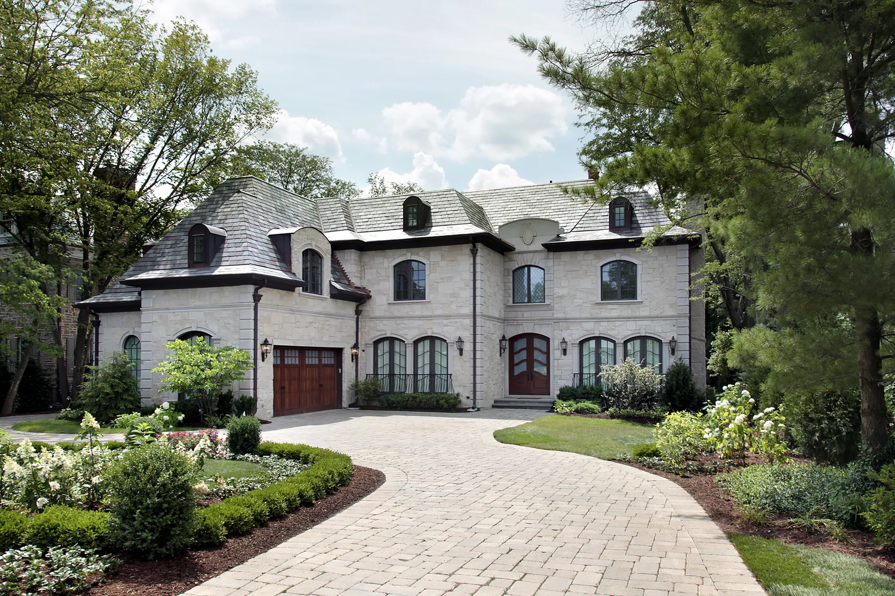 Large stone home with a landscaped front drive