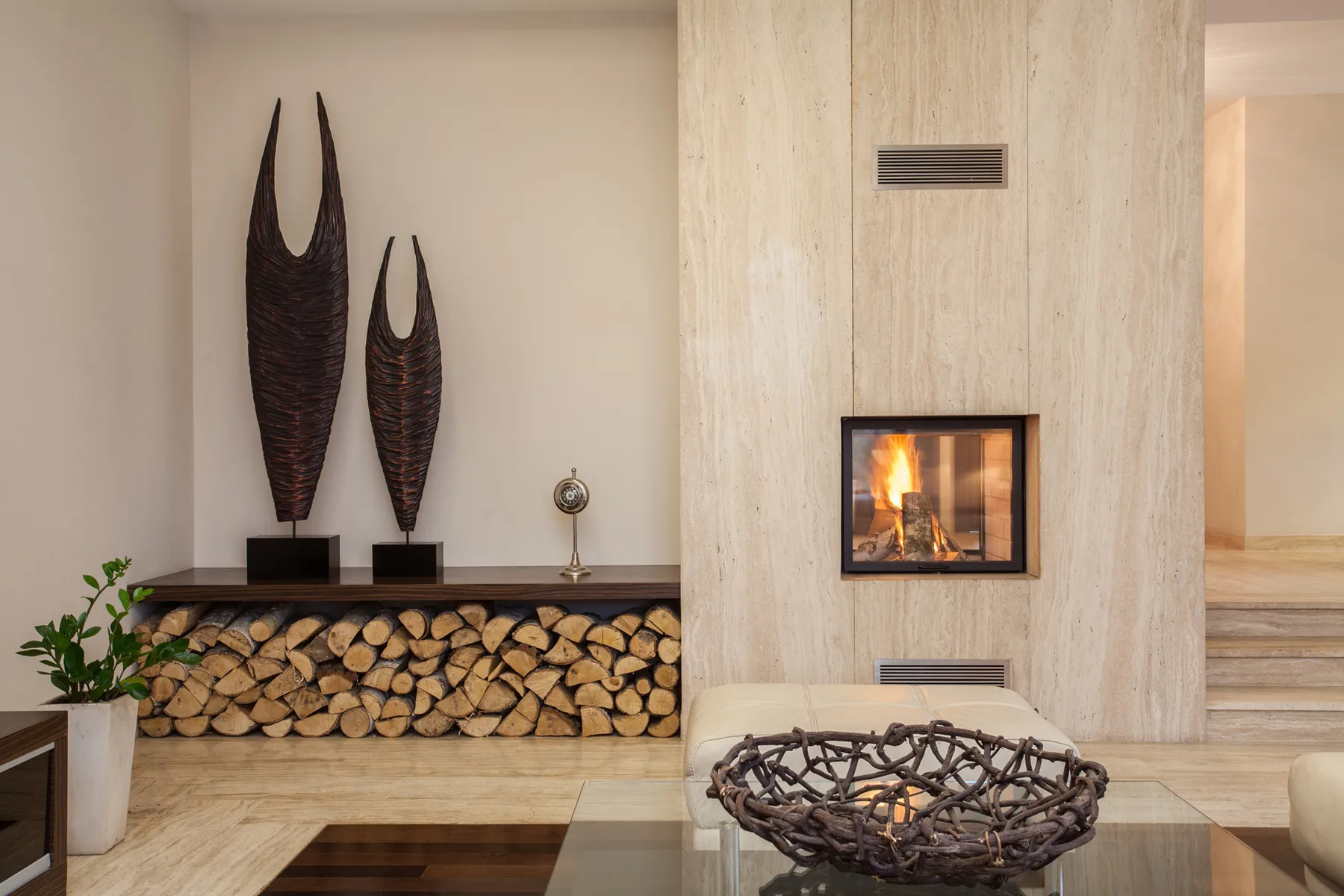 Modern stone fireplace beside stacked firewood and sculptural decor